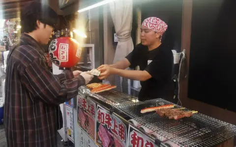Un cliente paga por comida callejera japonesa: brochetas de carne y surimi a la parrilla en un puesto.