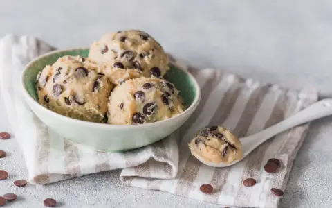 Schüssel mit köstlichem Cookie-Teig ohne Ei und Schokostückchen, bereit für den Ofen. Ein Löffel voll Teig liegt daneben.