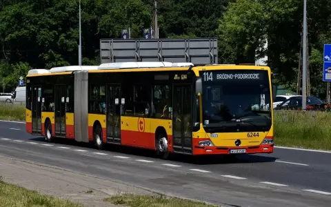 Autobus 114 jedzie ulicą w słoneczny dzień.