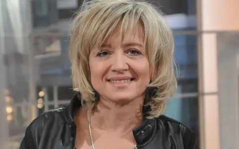 Uśmiechnięta Małgorzata Bogdańska w czarnej ramonesce, z blond włosami i delikatnym makijażem.
