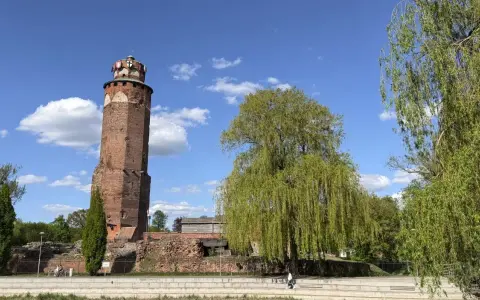Wieża zamkowa w Brodnicy, otoczona zielenią, na tle błękitnego nieba z chmurami. Piękny dzień na Pojezierzu Brodnickim.