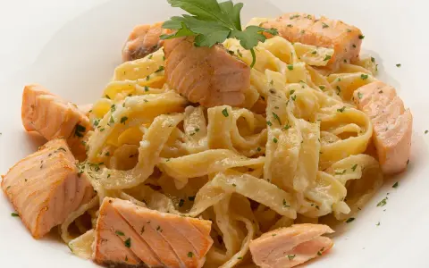 Deliciosa pasta con trozos de salmón rosado, cubierta con una cremosa salsa y espolvoreada con perejil fresco.
