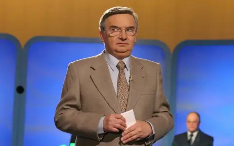 Tadeusz Sznuk, który prowadzi teleturniej Jeden z dziesięciu, w beżowej marynarce i z kartką w dłoni.
