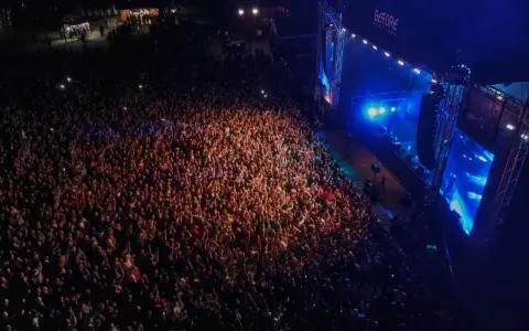 Tłum ludzi na koncercie, rozświetlony sceną i światłami. Atmosfera przed festiwalem Before Festival jest elektryzująca.
