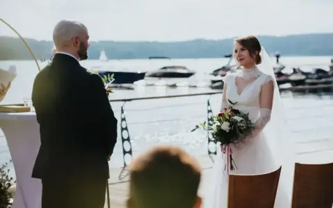Para Młoda podczas ceremonii ślubu kanonicznego nad jeziorem. Ona w białej sukni z bukietem, on w garniturze.