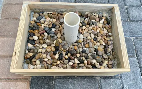 Base per ombrellone fai da te: un contenitore in legno riempito di ghiaia con un tubo centrale per l'asta.