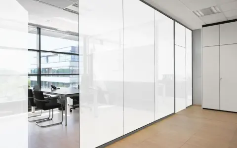 Oficina moderna con paredes de cristal que se oscurece, reflejando un edificio exterior y mobiliario de oficina.