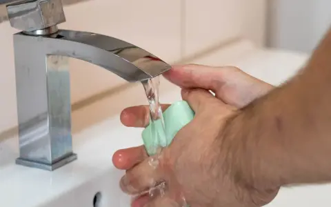 Mani che si lavano sotto un rubinetto cromato, con un getto d'acqua che indica una buona pressione dell'acqua dell'acquedotto.