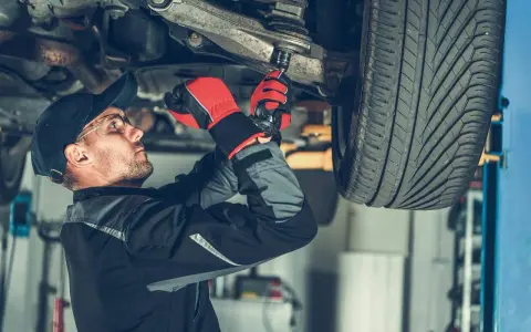 Mechanik w rękawicach dokręca sworzeń zwrotnicy w podwoziu samochodu.