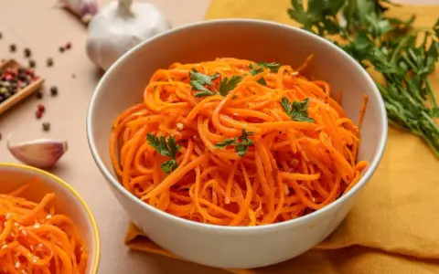 Aksamitna marchewka po koreańsku, udekorowana natką pietruszki, obok czosnku i kolorowego pieprzu.
