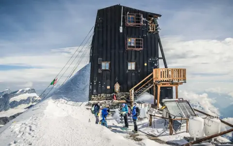 Die Capanna Margherita, eine Berghütte auf einem schneebedeckten Gipfel, mit Bergsteigern, die sich auf den Aufstieg vorbereiten.