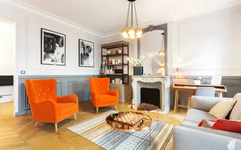Salon aux fauteuils orange vif, cheminée ornée, et un jeu d'échecs sur table basse, évoquant un mouvement baroque moderne.