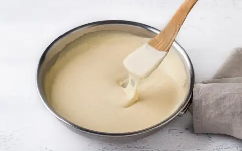 Una spatola di legno mescola una cremosa fonduta di parmigiano in una padella.