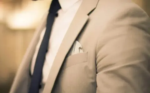 Elegancki mężczyzna w jasnej marynarce i granatowym krawacie. Zastanawiasz się, ile zarabia manager hotelu?