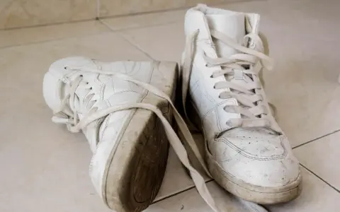 Par de zapatillas blancas sucias, con cordones desatados, sobre baldosas. Aprende como secar zapatillas blancas para que no se pongan amarillas.