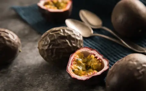 Reife Passionsfrüchte, eine aufgeschnitten, zeigen ihr saftiges Inneres. Zwei Löffel liegen bereit, um die exotische Frucht zu genießen.