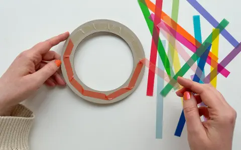 Hände bereiten einen Ring für Fenstersterne vor, indem sie bunte Streifen zum Falten bereitlegen.