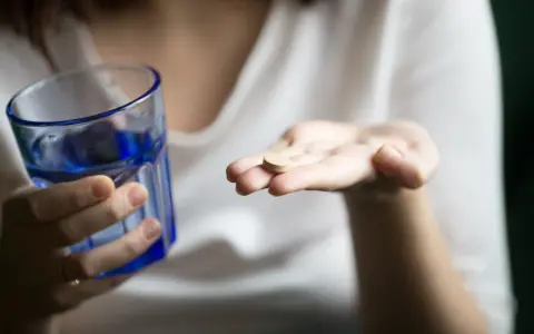 Une main tient un comprimé, peut-être un supplément de sels minéraux, à côté d'un verre d'eau bleue.