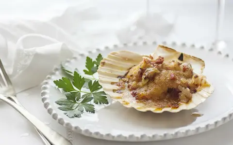 Vieiras a la gallega, un manjar en su concha, adornado con perejil fresco sobre un plato blanco.