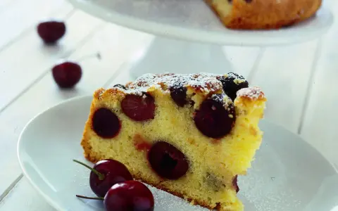 Una fetta di torta soffice e dorata, ricca di ciliegie succose, cosparsa di zucchero a velo. Perfetta per un momento di dolcezza.