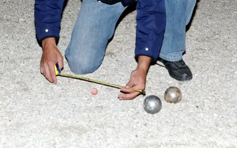 Un joueur de pétanque mesure la distance entre les boules. On se demande combien gagne un joueur de pétanque professionnel.
