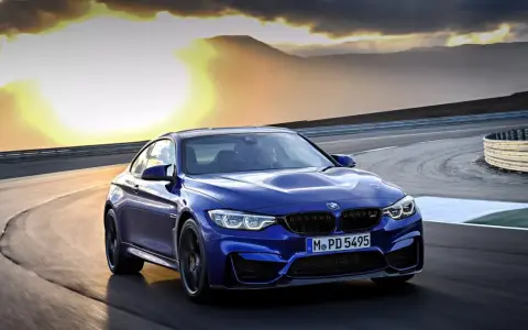Niebieskie BMW M2 CS pędzi po torze wyścigowym podczas zachodu słońca.