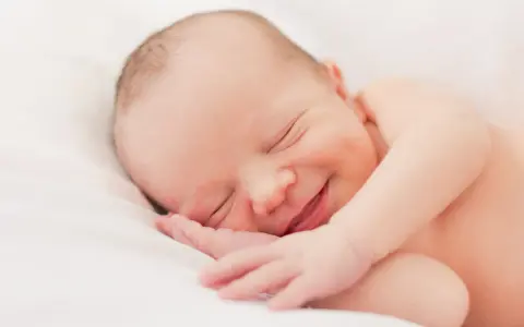 Un bebé duerme plácidamente, con una sonrisa que nos hace preguntar porque sonrien los bebes. Su carita refleja paz y felicidad.