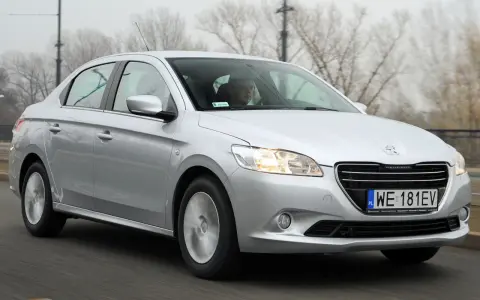 Srebrny Peugeot 301 jedzie po drodze, za kierownicą siedzi mężczyzna w okularach.
