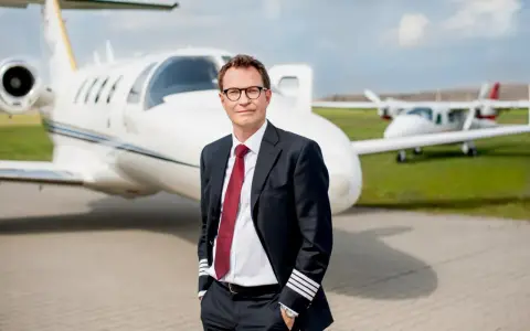 Pilot w garniturze z odznaką na rękawie, stojący przed odrzutowcem. Zastanawiasz się, ile zarabia pilot Ryanair?