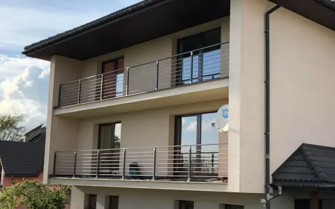 Nowoczesny dom z dwoma balkonami, gdzie zamiast tradycyjnej balustrady zastosowano elegancki murek z poziomymi stalowymi elementami.