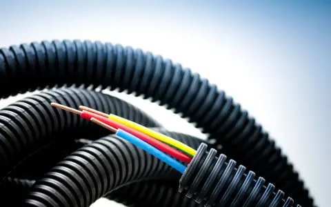 Trois fils électriques colorés sortent d'un tube plastique souple noir et ondulé, prêt à protéger les câbles.