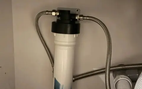 Système de filtration d'eau sous évier avec un cartouche charbon actif blanc et noir, relié par des tuyaux flexibles.