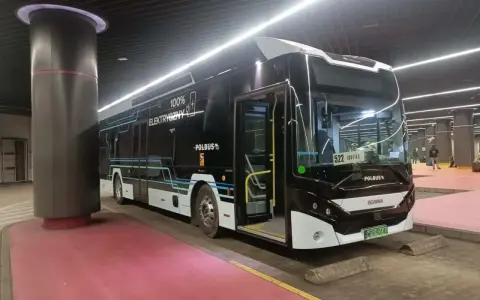 Nowoczesny, czarny autobus elektryczny z napisem "100% ELEKTRYCZNY" stoi na przystanku.