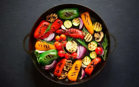 Un assortimento colorato di verdure grigliate, tra cui peperoni, zucchine, pomodorini, cipolle rosse e funghi, disposte in una padella scura.