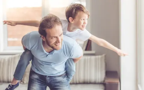 Ein Vater trägt seinen Sohn auf dem Rücken. Der Sohn streckt die Arme aus wie ein Flugzeug. Das sind meine worte an meinen sohn: Flieg hoch!
