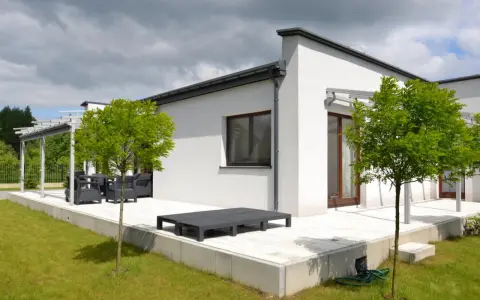 Nowoczesny biały dom z płaskim dachem, tarasem i zielonym ogrodem.