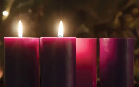 Two lit candles glow on the 2nd Sunday of Advent, their flames casting a warm light on the surrounding purple and pink candles.