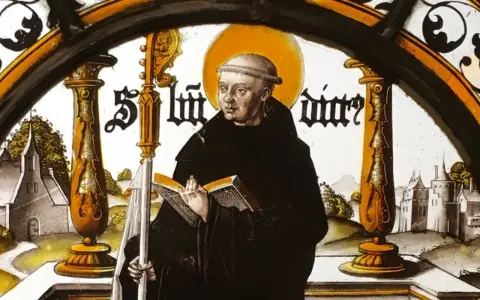Stained glass depicting St. Benedict the Abbot, holding a book and staff, with a monastery in the background.