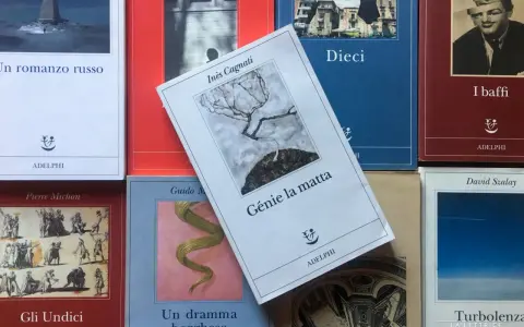 Libri Adelphi in primo piano, tra cui "Génie la matta" di Inès Cagnati, con un albero spoglio su sfondo grigio.