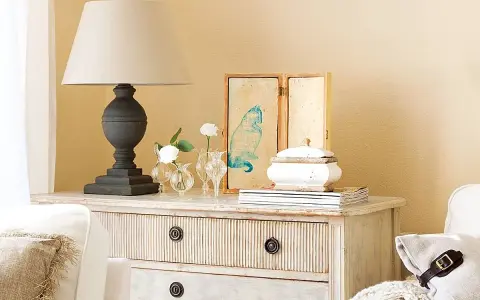 Cómoda de estilo vintage con cajones pintados a la tiza, decorada con lámpara, jarrones con flores y un cuadro de gato.