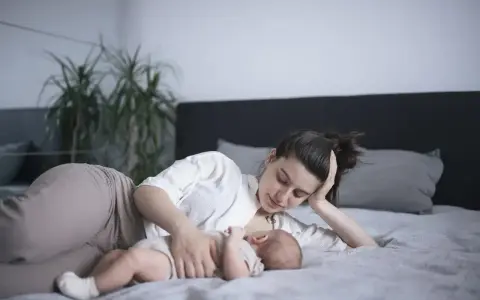Matka karmi piersią dziecko na leżąco, opierając głowę na dłoni. Czuły moment bliskości.