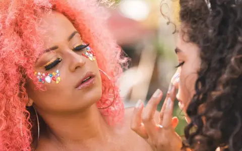 Kolorowy makijaż na festiwal z brokatem i kamyczkami. Różowe włosy i błyszczące oczy.