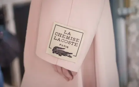 Różowy płaszcz z metką "LA CHEMISE LACOSTE PARIS" z krokodylem, symbol luksusowych marek ubrań.