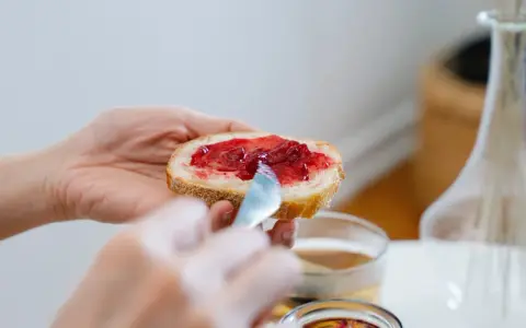 Hände verteilen Marmelade auf Brot. Ein süßer Genuss, der an die besonderen Gelüste in der Schwangerschaft erinnert.