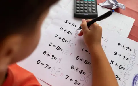 Dziecko zmagające się z zadaniami matematycznymi, być może z dyskalkulią. Widoczne są próby rozwiązań i poprawki.