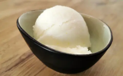 Ein Löffel cremiges Sorbet ohne Zucker in einer stilvollen Schale auf Holzhintergrund. Erfrischend und leicht.