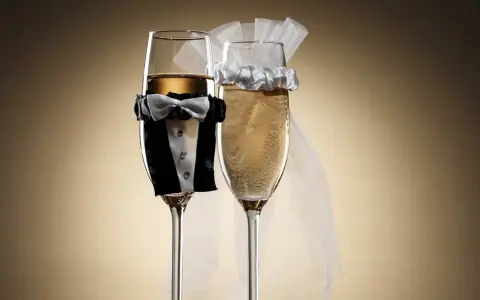 Dwa kieliszki szampana, jeden w stroju pana młodego, drugi z welonem panny młodej. Idealne wino dla pary młodej na toast.