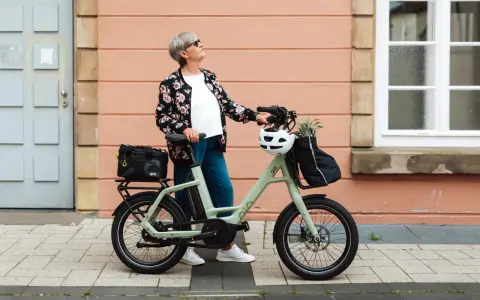 Ältere Dame mit QIO Bike, positive Erfahrungen mit dem E-Bike, das mit einem Helm und einer Tasche beladen ist.