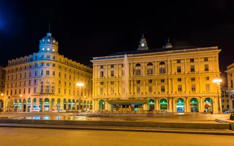 Piazza De Ferrari illuminata di notte, con la fontana centrale e gli edifici storici che animano la vita notturna di Genova.