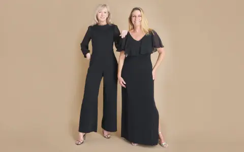 Two women in elegant black evening attire, a wide-leg jumpsuit and a flowing gown, ready for a formal event.